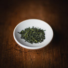 White bowl with green tea leaves on a wooden surface