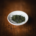 White bowl filled with green tea leaves on a wooden surface