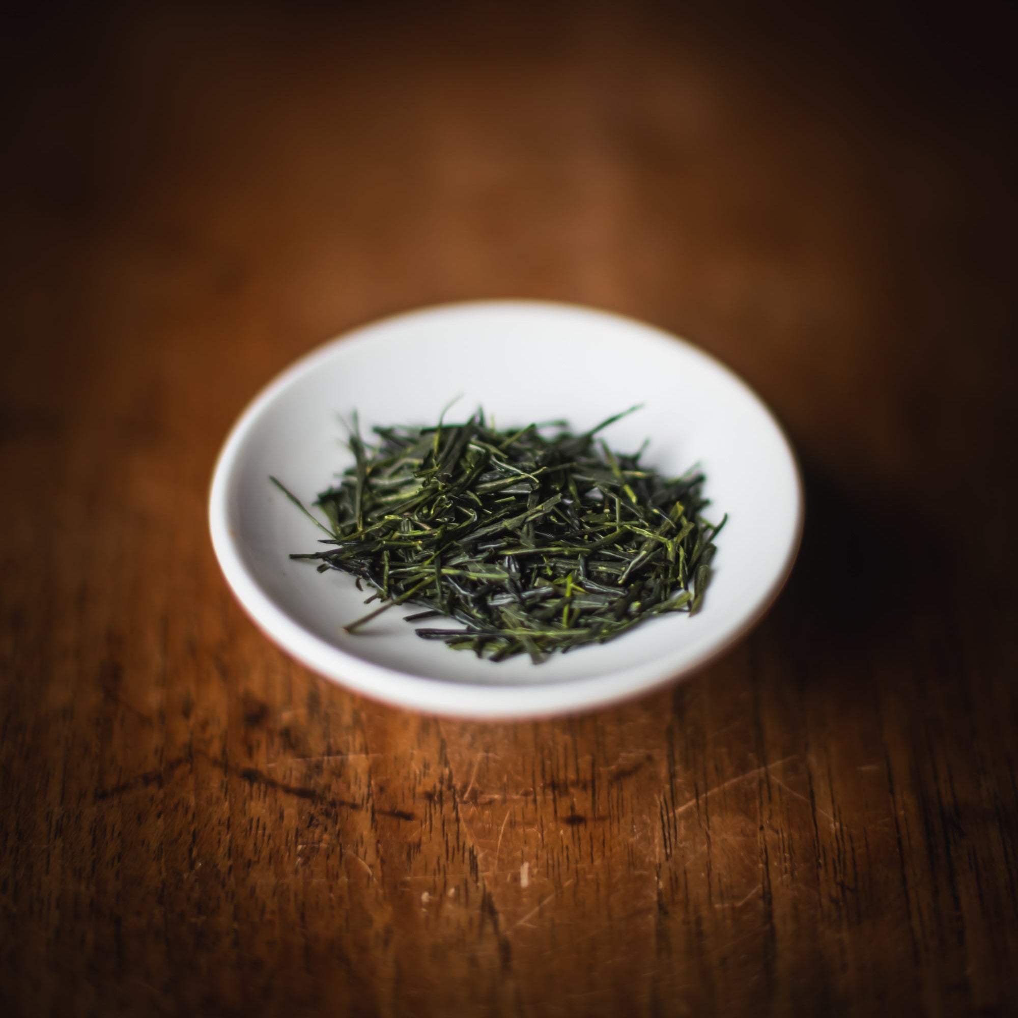 White bowl filled with green tea leaves on a wooden surface