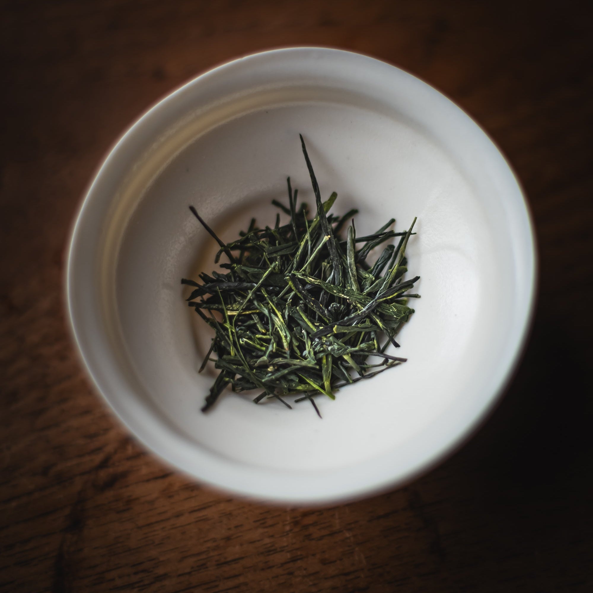 White bowl with green tea leaves on a wooden surface