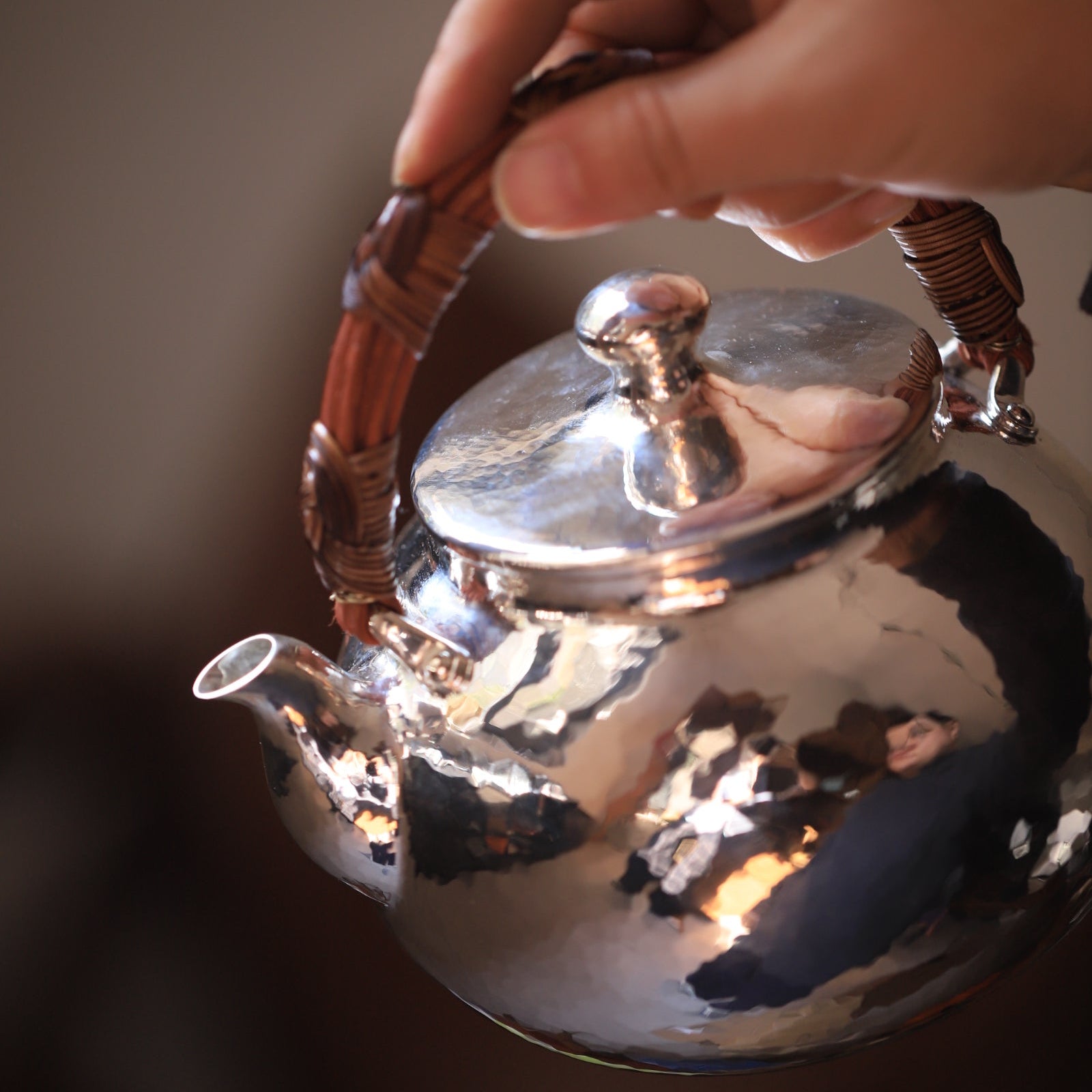 Hand holding a shiny silver teapot with a blurred background