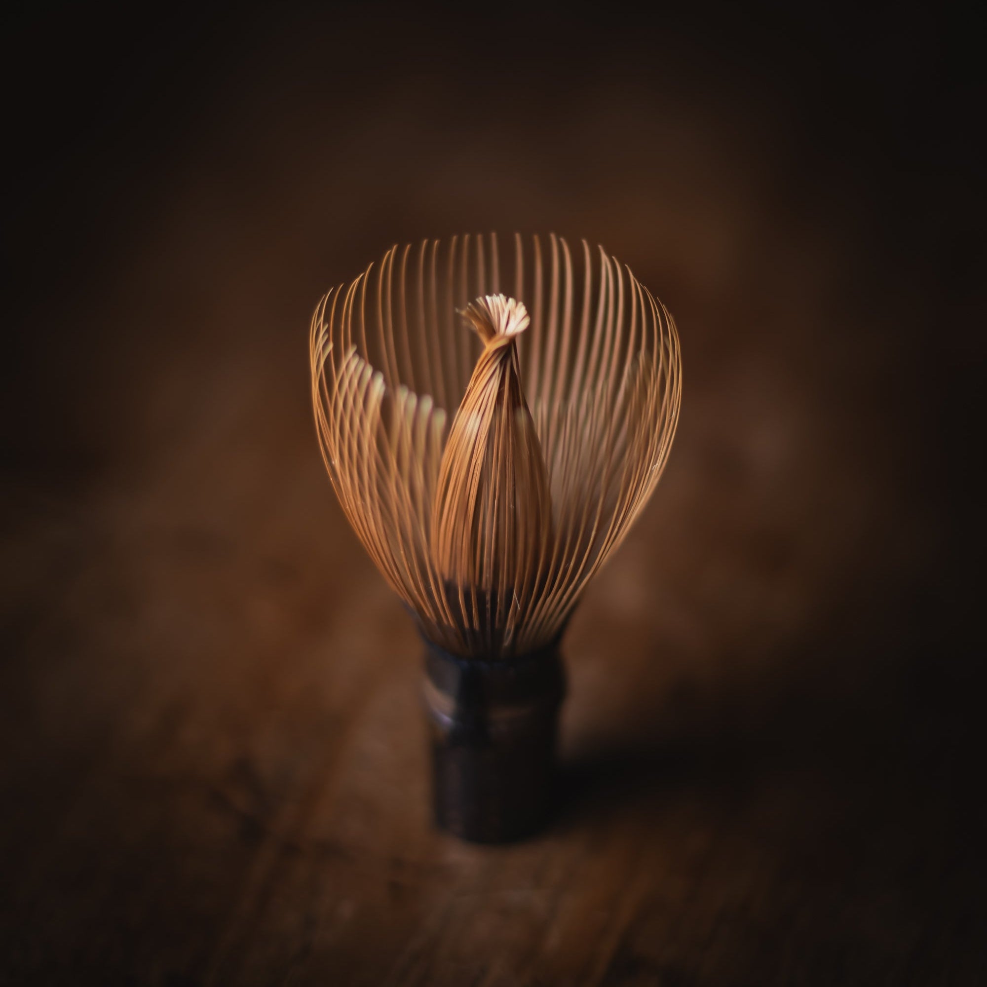 Traditional Japanese whisk (chasen) on a wooden surface with a dark background