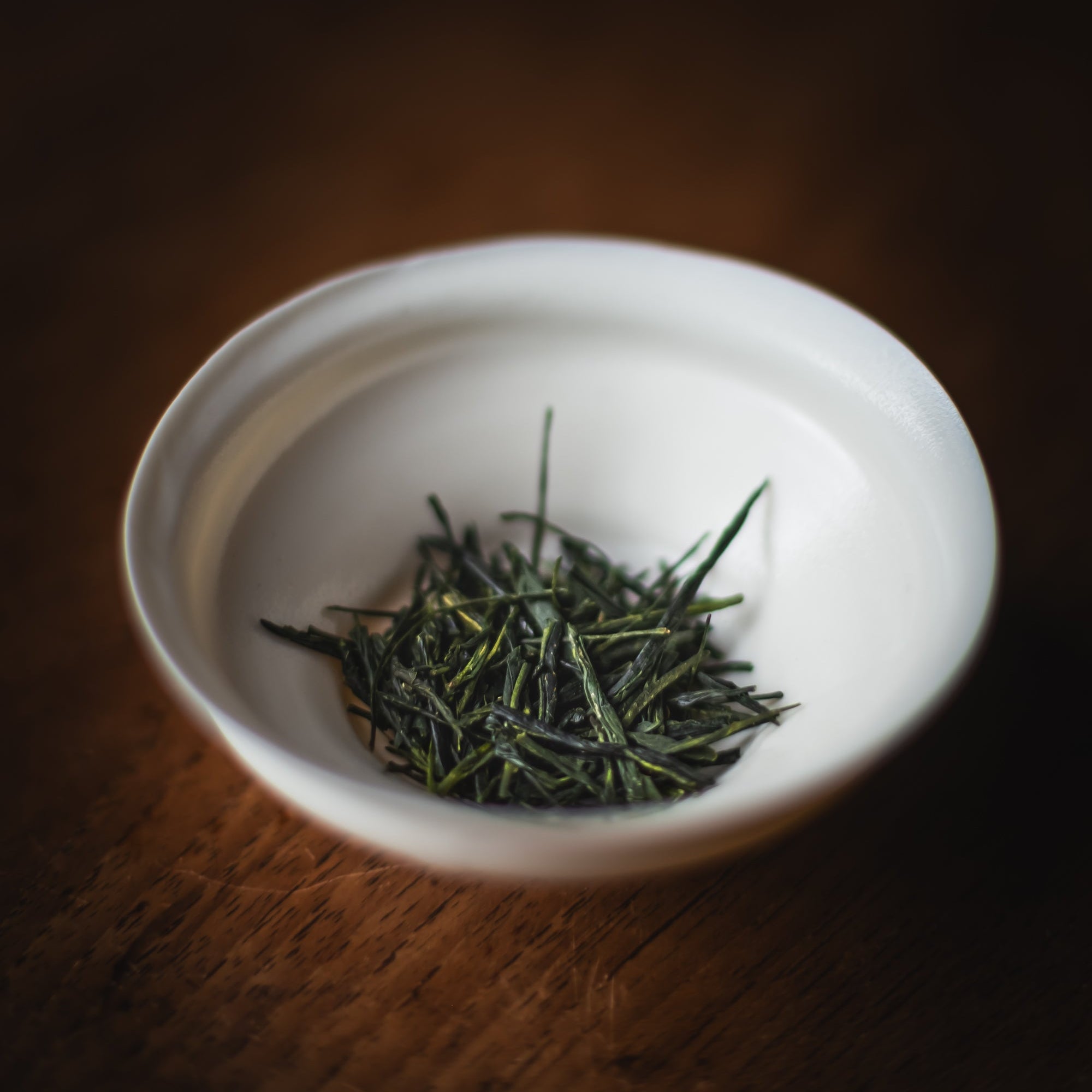 White bowl with green tea leaves on a dark wooden surface