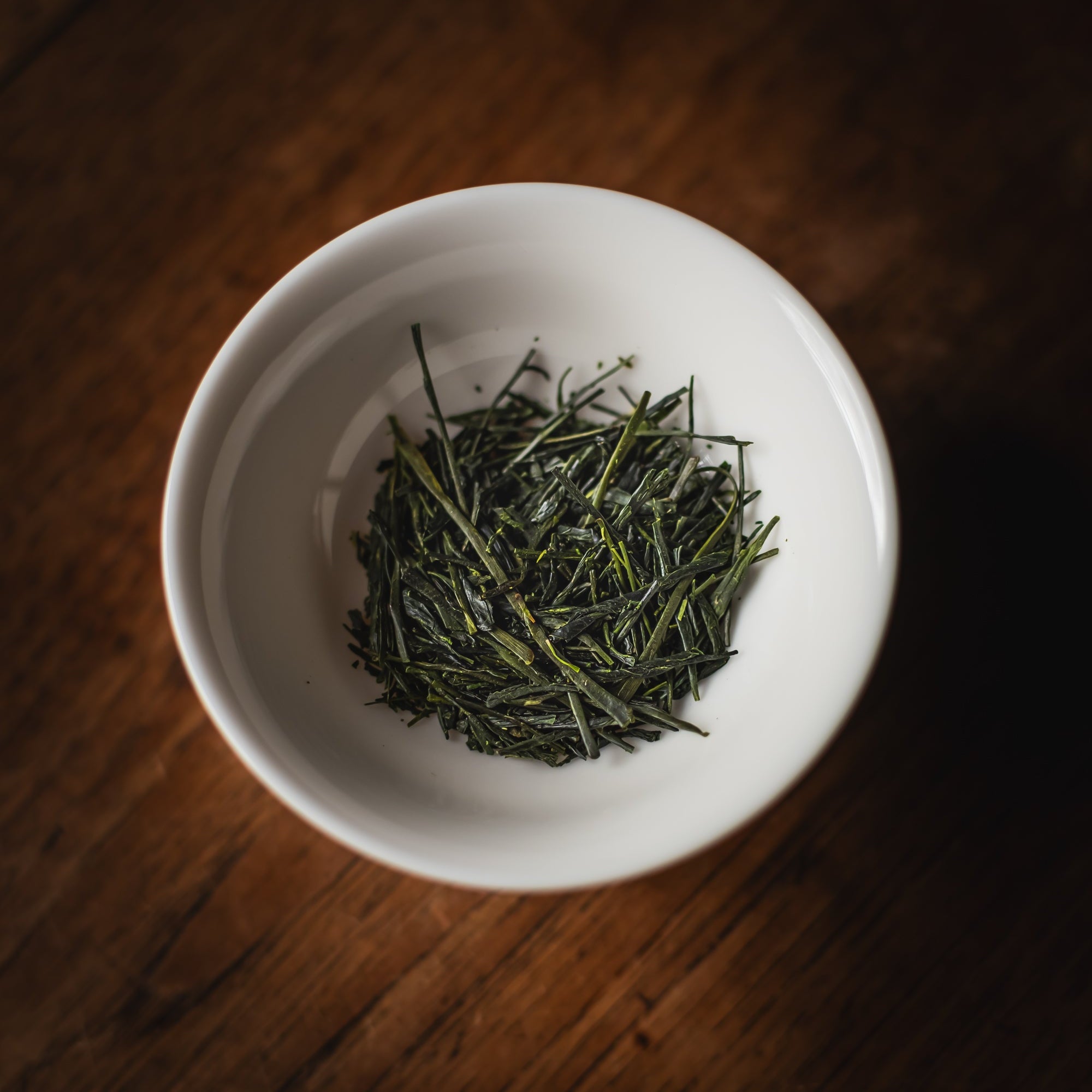 White bowl filled with green tea leaves on a wooden surface