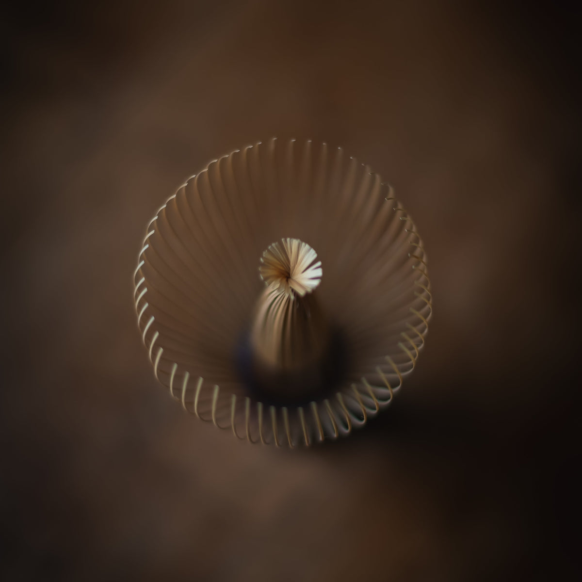 A top-down view of a beige ribbed plastic cup with a flared rim and a small textured center, set against a dark brown gradient background.