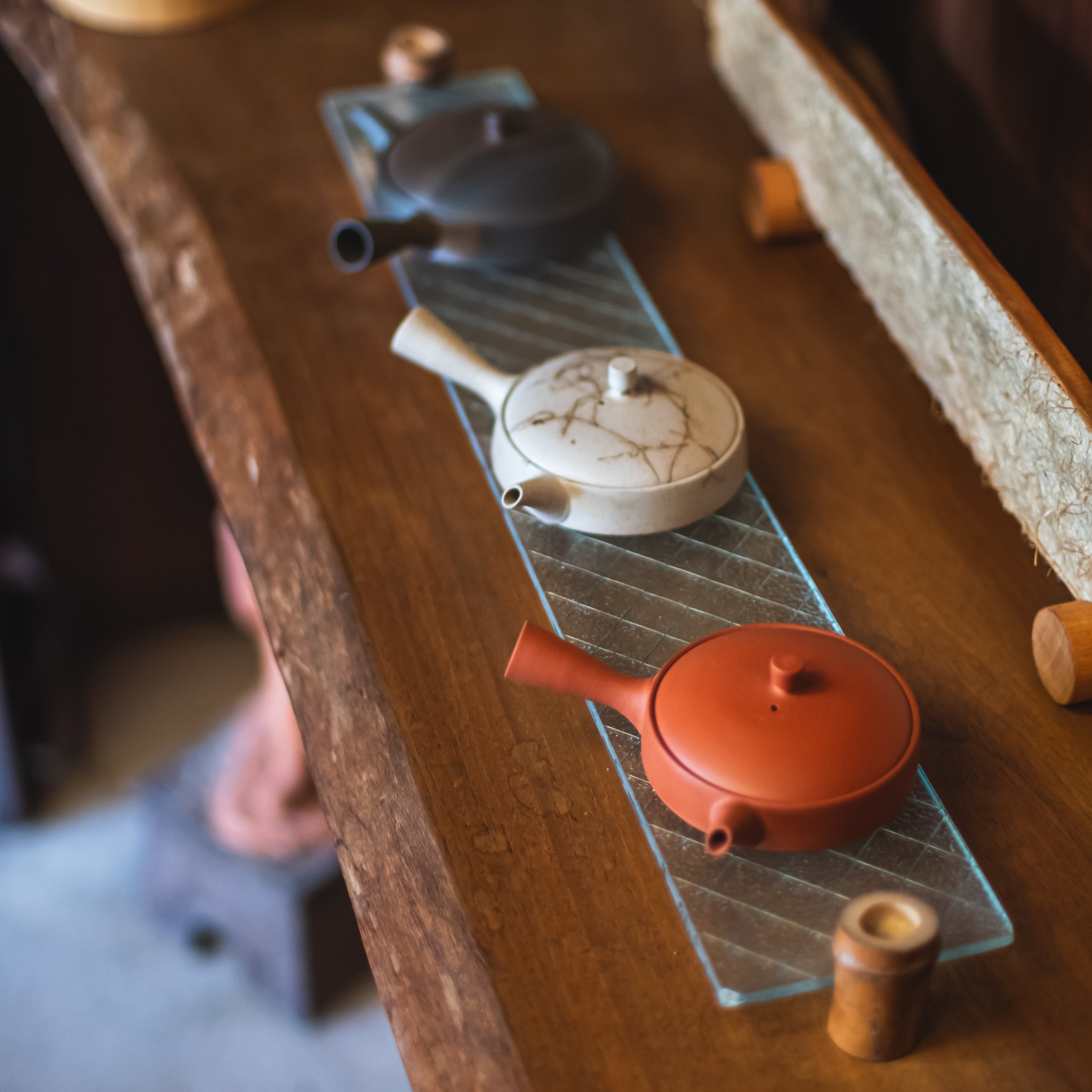 Hira Kyusu flat side-handle teapots on a glass tray with wooden surface and blurred background.