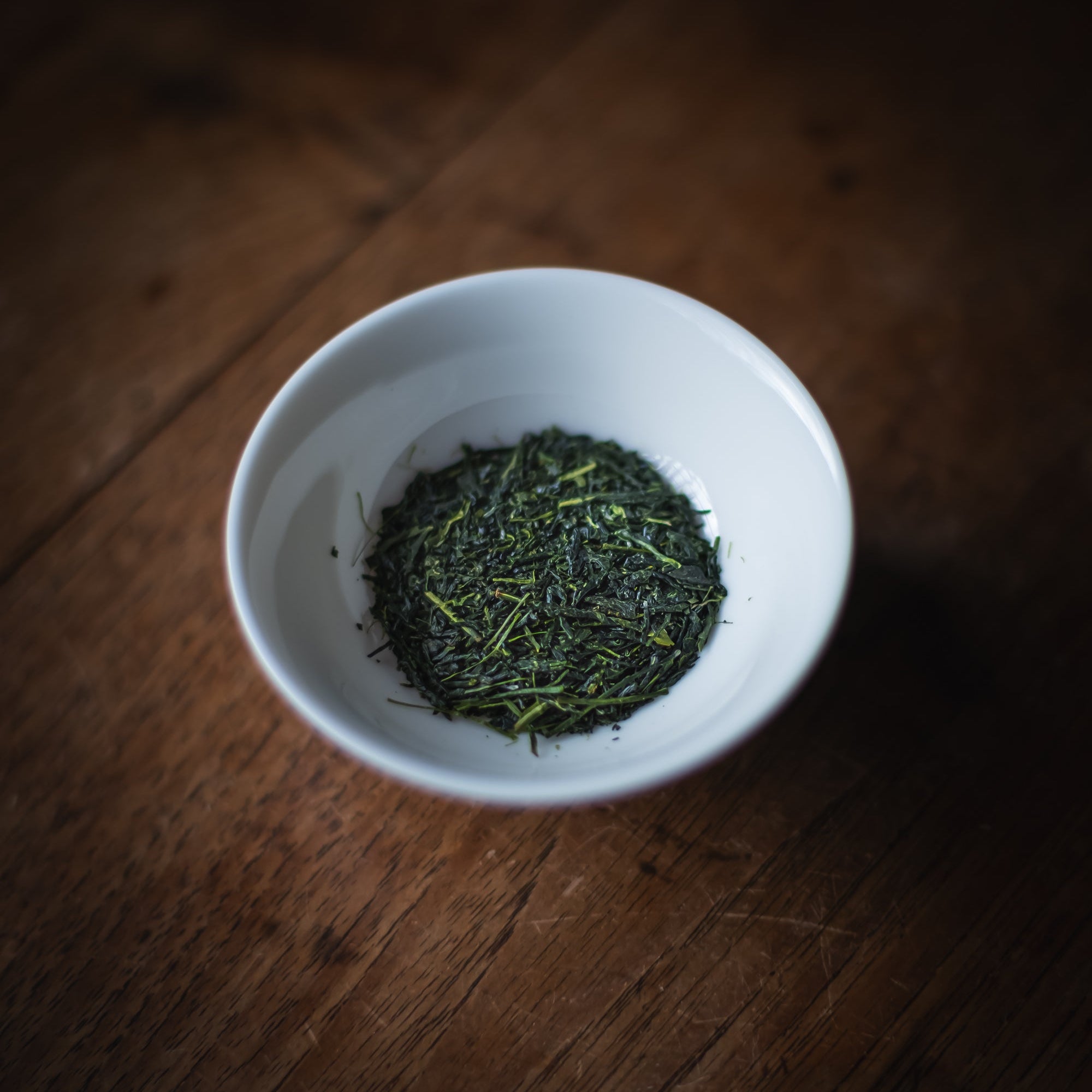 White bowl filled with sencha leaves on a wooden surface