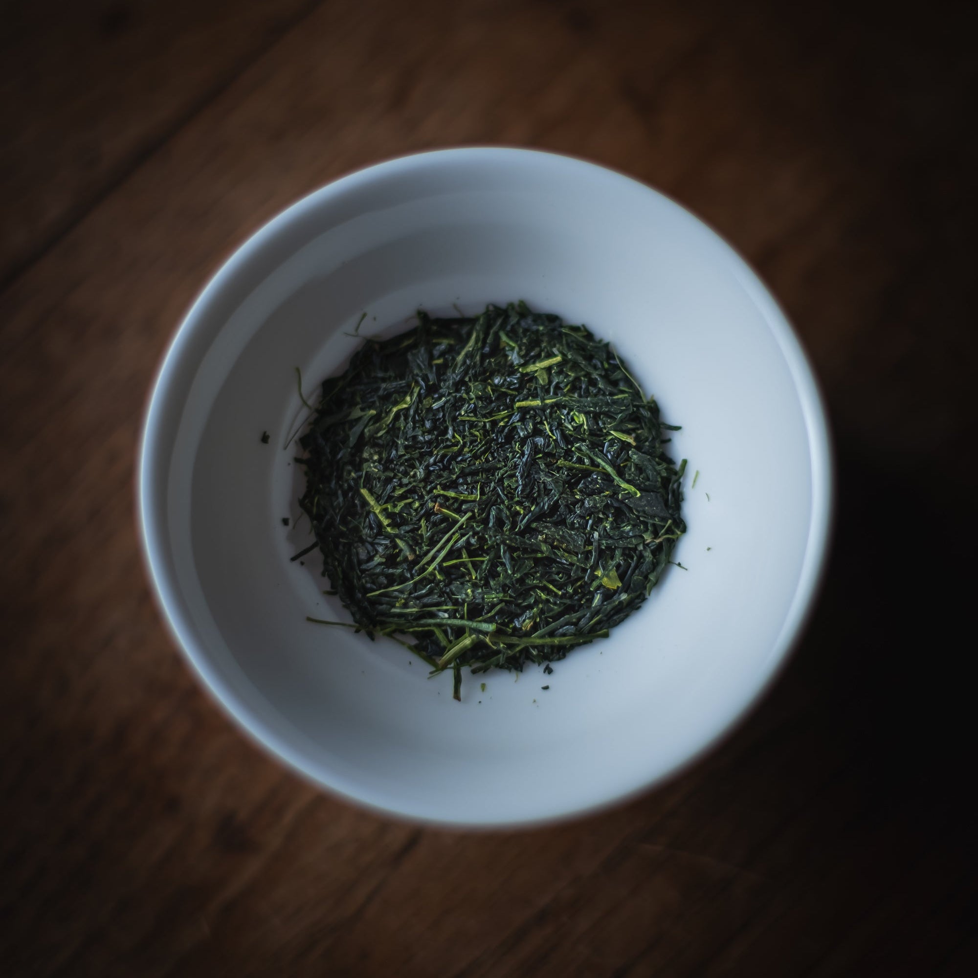 White bowl filled with Sencha leaves on a wooden surface