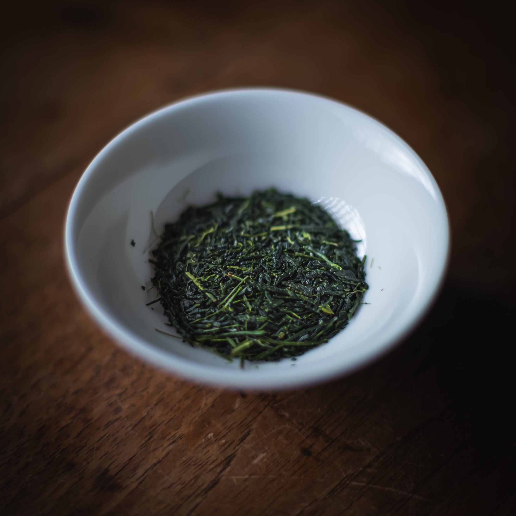 White bowl filled with green tea leaves on a wooden surface