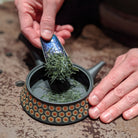 Person adding tea to a small pot on a textured surface